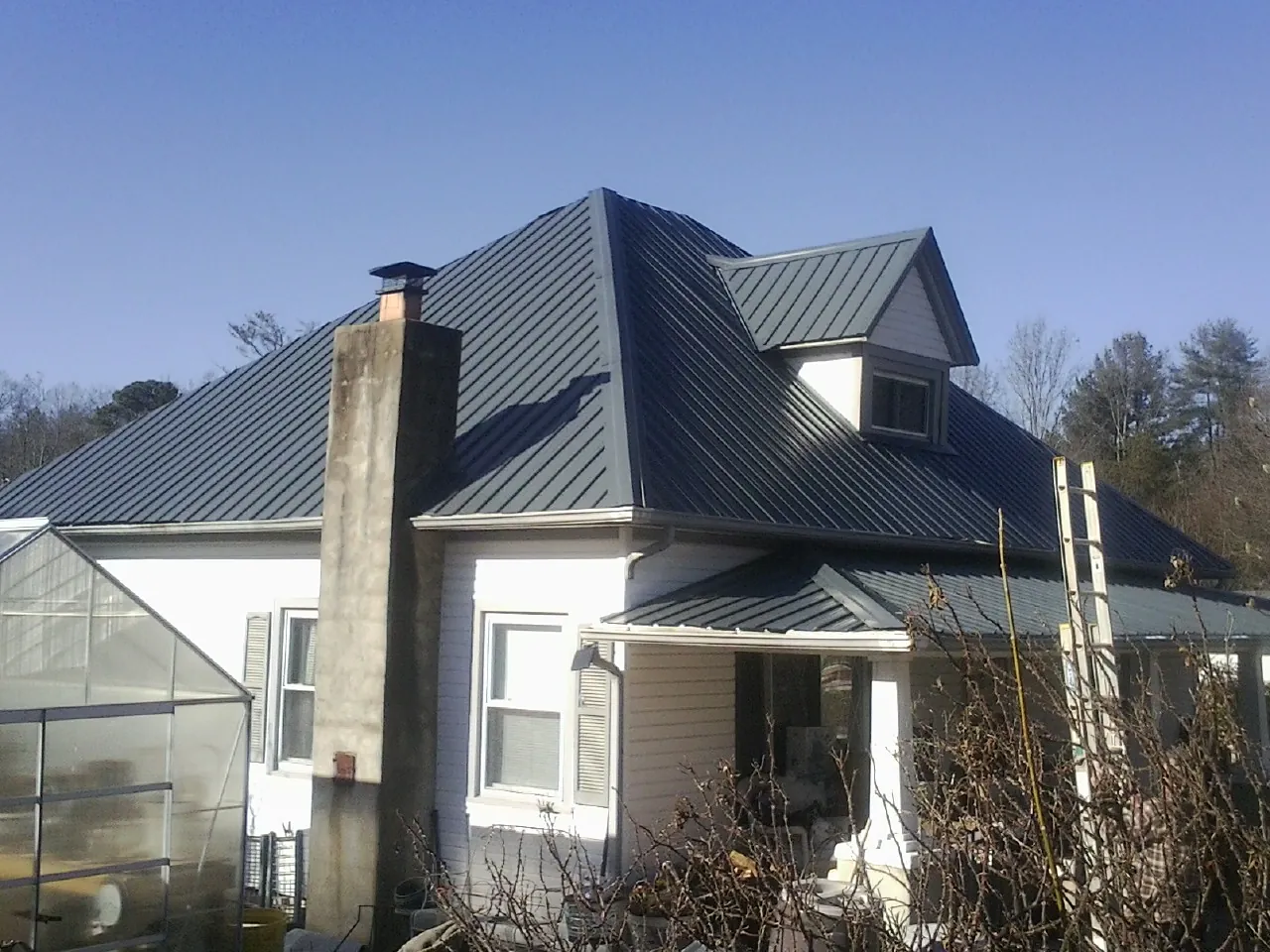 Dark blue standing seam metal roof on a white farmhouse with dormer — Slate & Tile Roof Repair by Roofing Brothers in Dunnsville