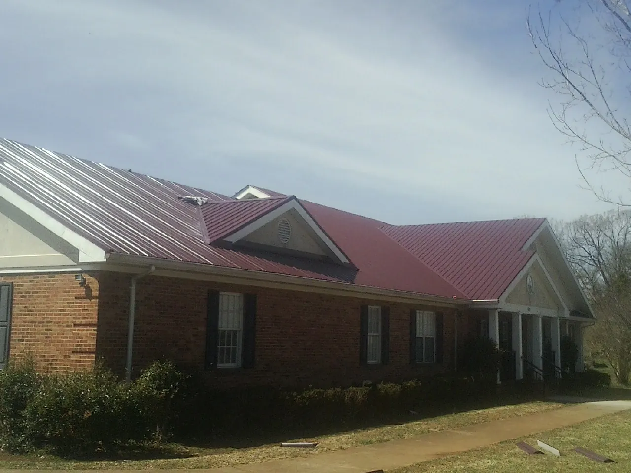 Red metal roof with gabled entries on a long brick building, from a Hail Damage Roof Repair job in Dunnsville