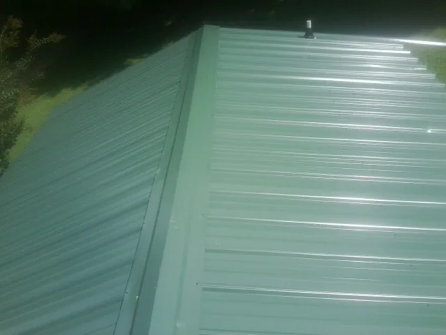 New green metal panels meeting at the ridge of a roof — Flat Roof Repair work by our crew in Dunnsville