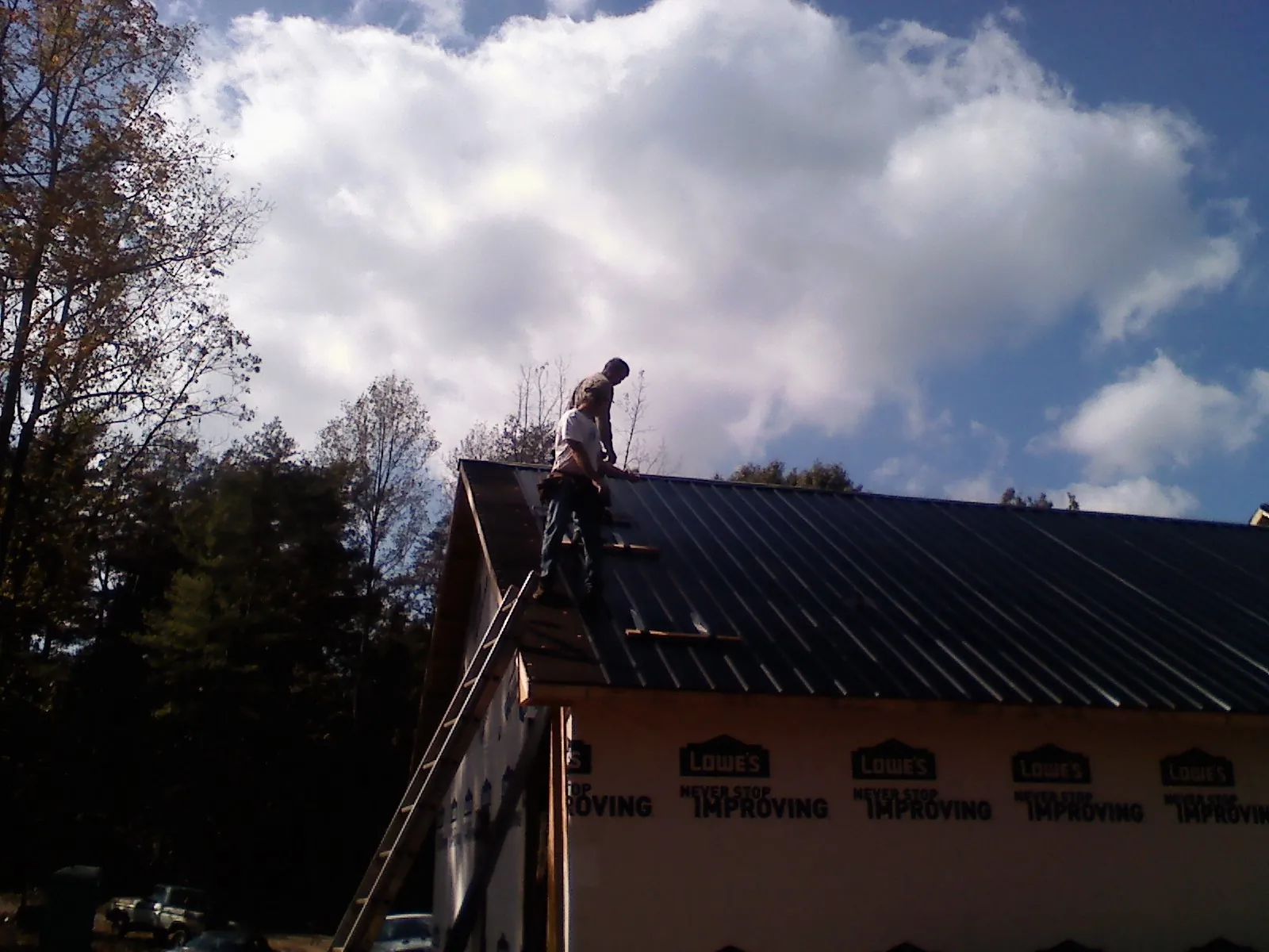 Roofer fastening dark metal panels high against a cloudy sky, from a Roof Inspection job in Dunnsville