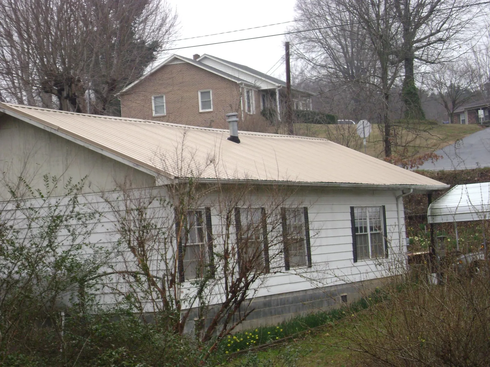 Tan metal roof on a white sided house set into a hillside — Commercial Roofing by Roofing Brothers in Dunnsville