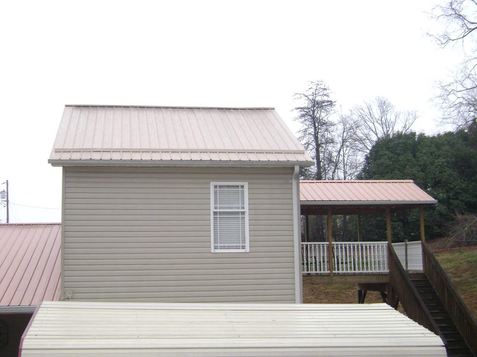 Tan metal roofs on a two story addition and attached porch, from a Roof Replacement job in Dunnsville